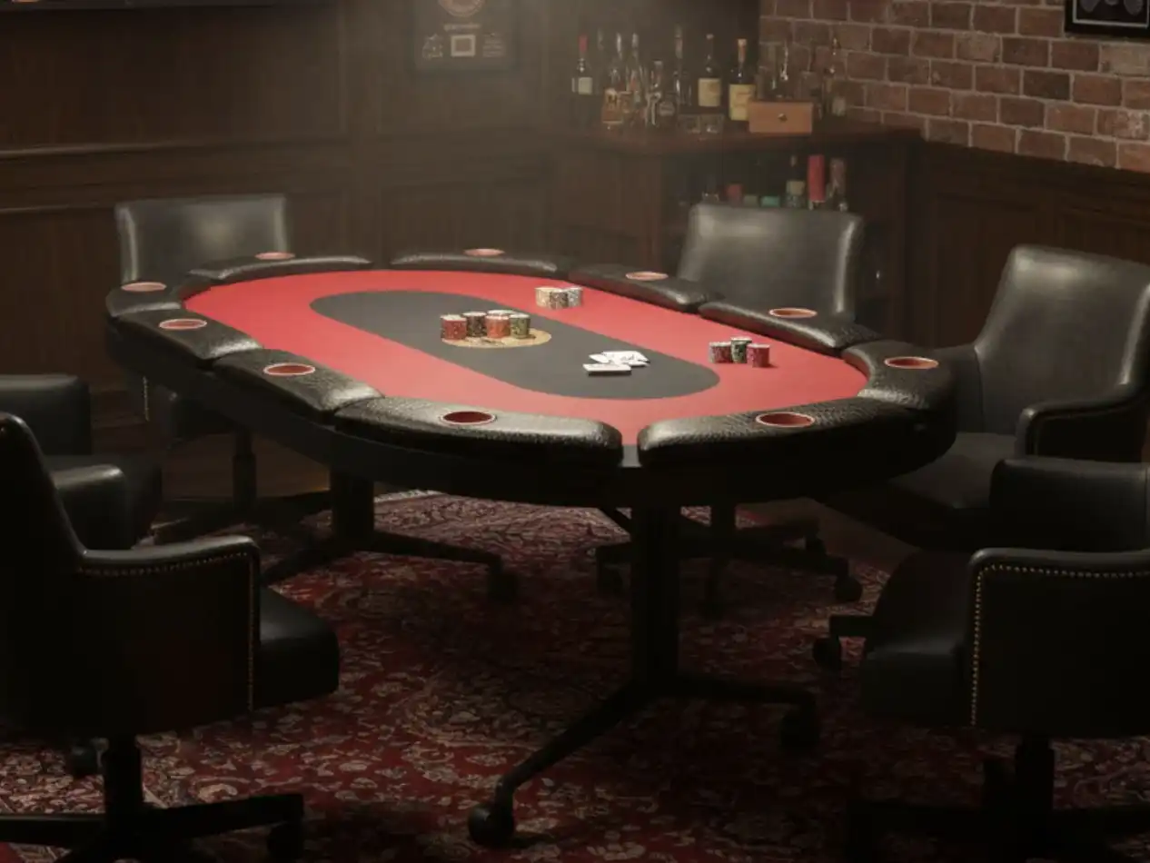 Premium 10-player poker table with red felt, black leather armrest with cup holders, and a pedestal base, shown in a rustic brick-walled game room.