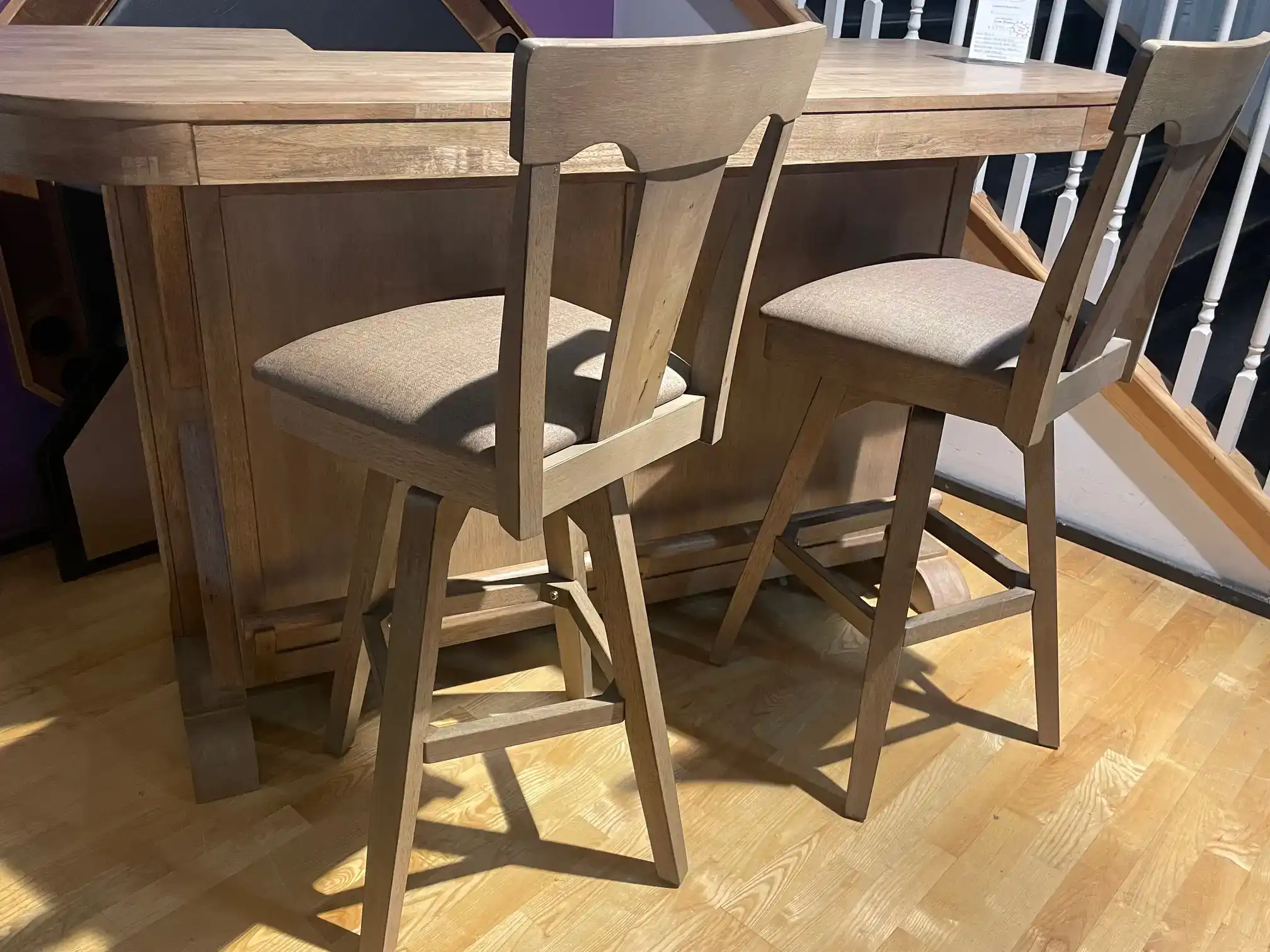 Two light oak swivel bar stools with upholstered cushioned seats sit at a matching wooden home bar counter on hardwood flooring.