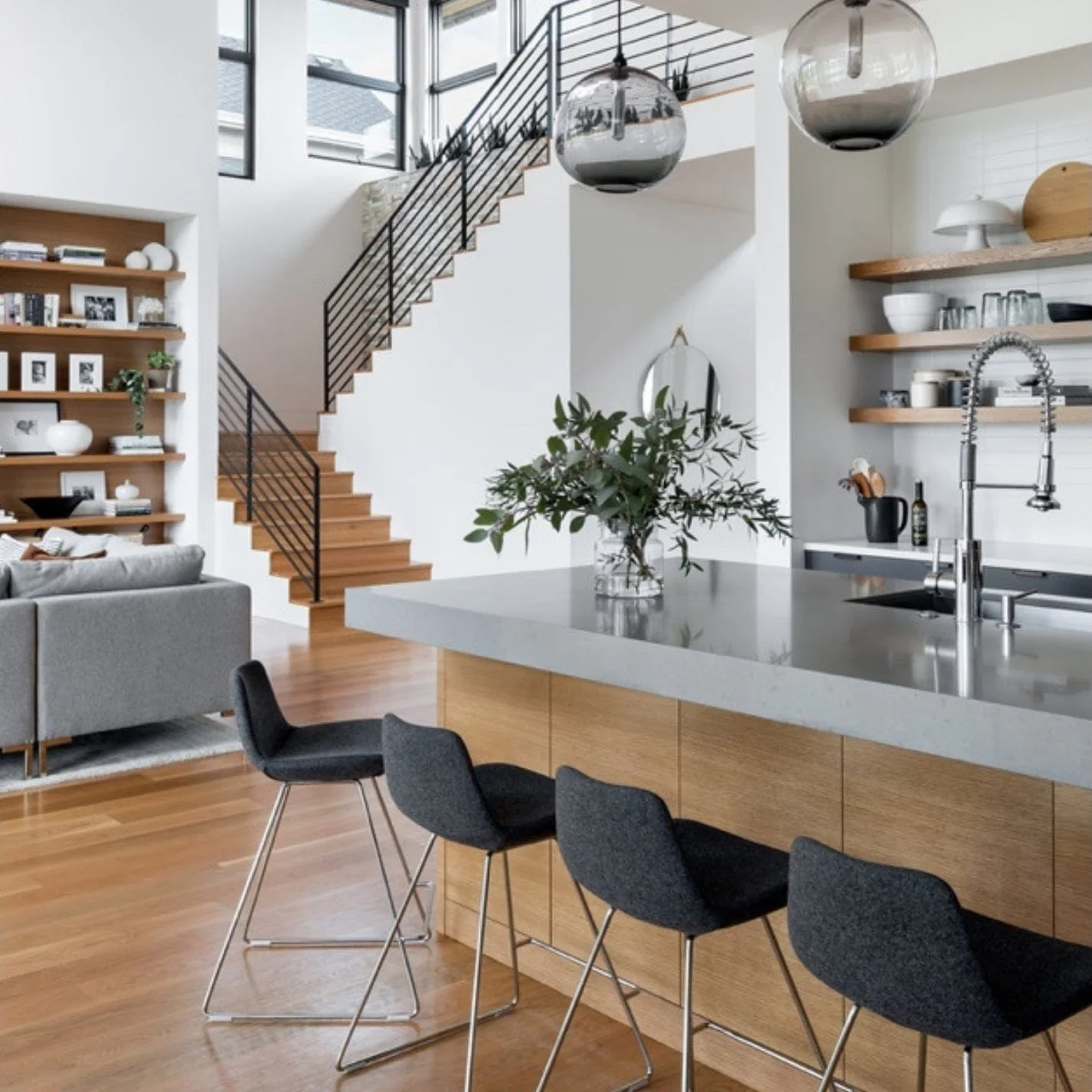 Modern kitchen island featuring a light wooden base, grey countertop, and four dark grey fabric bar stools set in an open-concept interior.