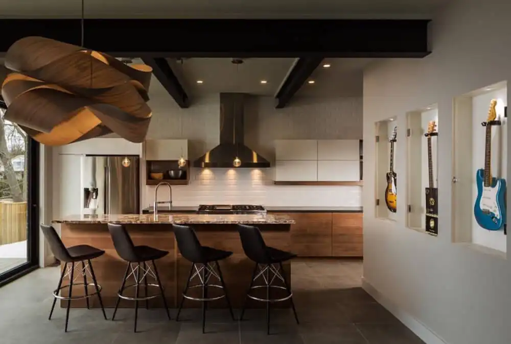 Modern kitchen with a wooden island, four black leather bar stools, dark ceiling beams, and wall-mounted guitars displayed in recessed niches.