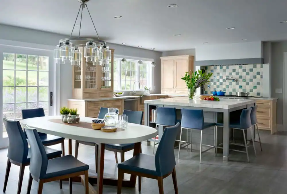 pacious open-concept kitchen and dining area featuring blue upholstered chairs around an oval table and matching blue bar stools at the island.
