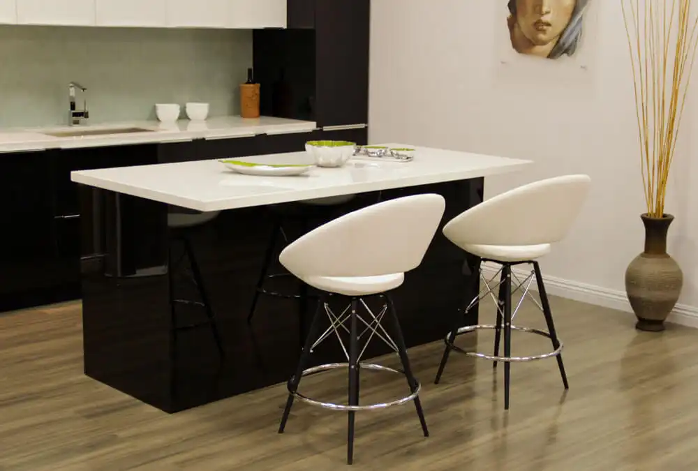 Modern kitchen with a wooden island, four black leather bar stools, dark ceiling beams, and wall-mounted guitars displayed in recessed niches.
