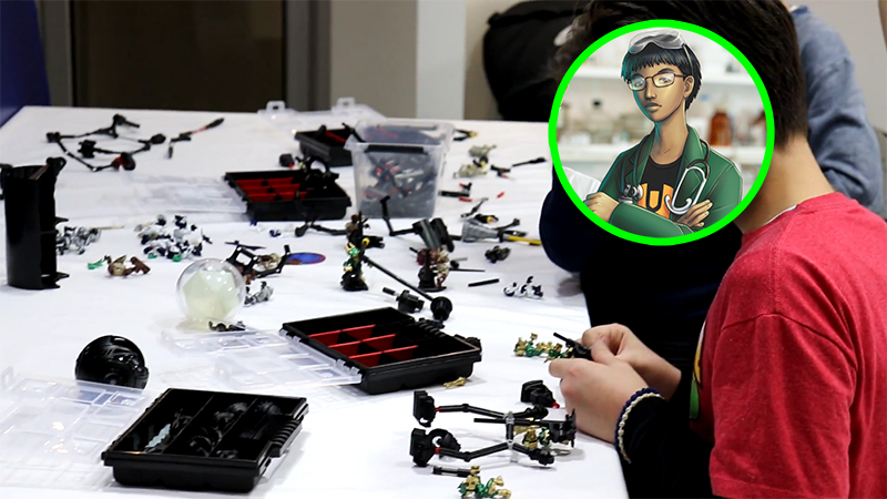 Photo of a young boy sat at a large table with a range of Temari mech components on it, he is assembling some parts and his face is covered by a circular NAN avatar.