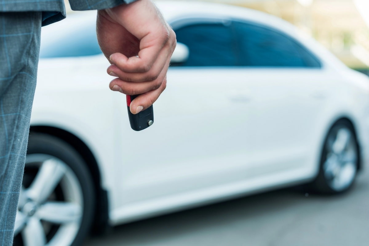 Hand holding car keys in front of a white vehicle during pickup or delivery.