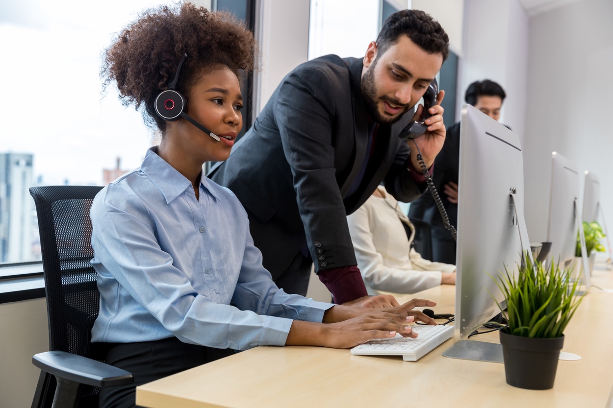 Sales manager providing training to agent with headset by listening in during phone conversation