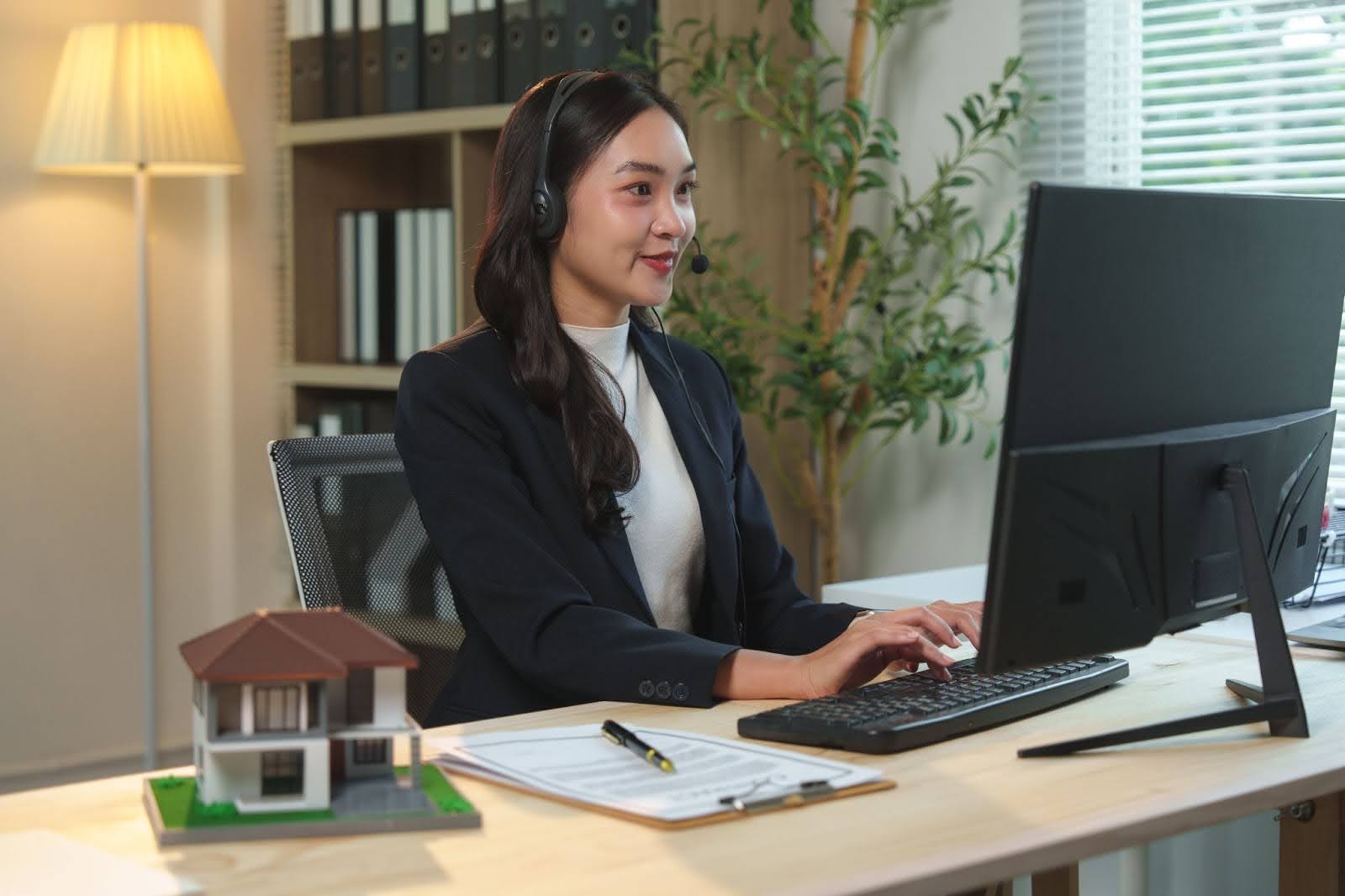 Sales agent with model house on desk selling mortgage over phone using free script generator and PhoneBurner