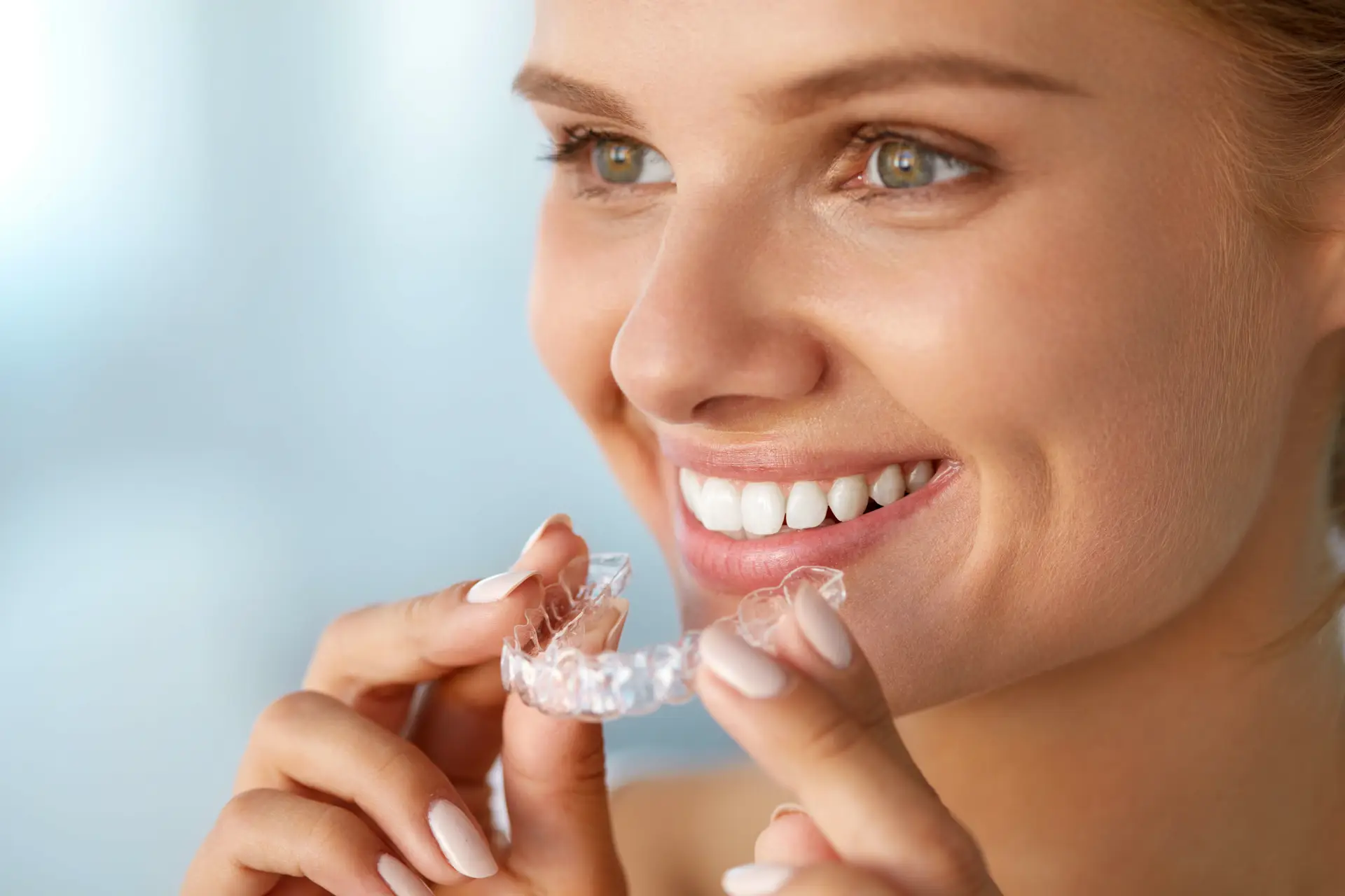 Smiling woman holding a clear Invisalign aligner in Staten Island