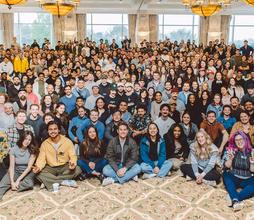 Large diverse group of people posing indoors in multiple rows, smiling and facing the camera.