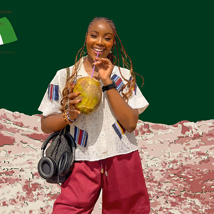Woman with braided hair holding a coconut and drinking with a straw, smiling at the camera.