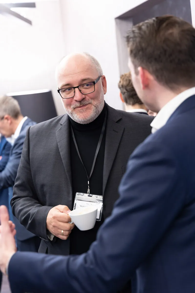 Mann hält weiße Kaffeetasse und unterhält sich mit seinem Kollegen
