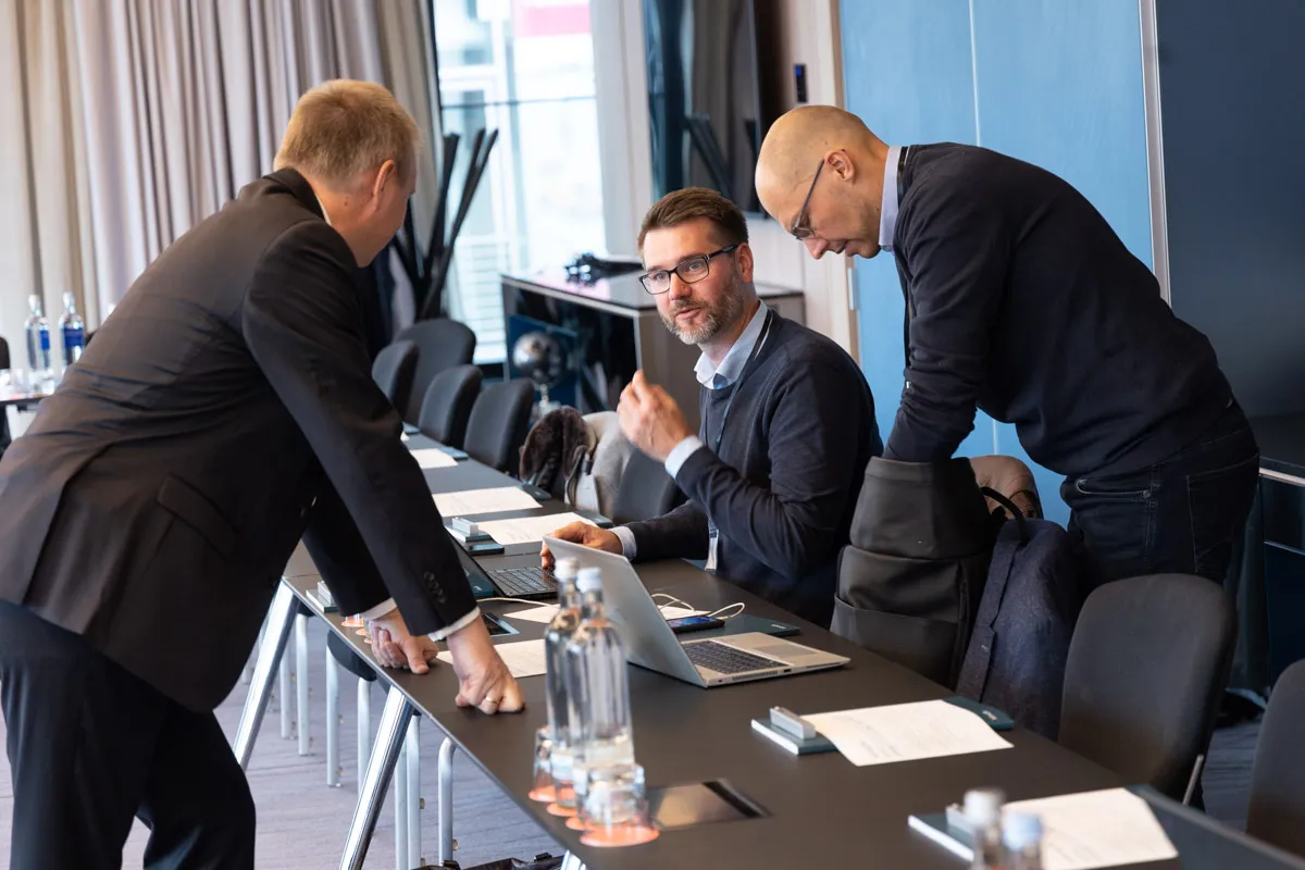 Mann stützt sich auf Meetingtisch und unterhält sich mit Kollegen