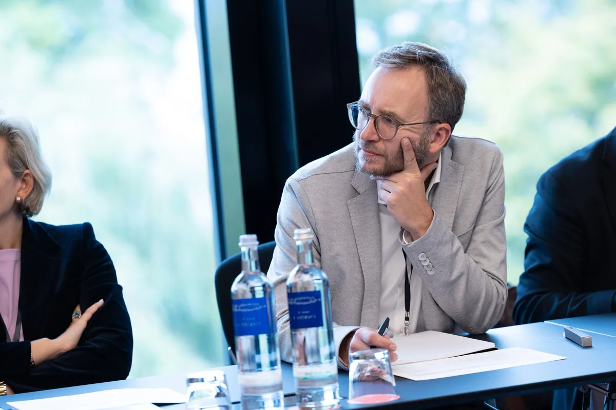 Mann im beigen Anzug stützt Gesicht auf die Hände und hört im meeting zu