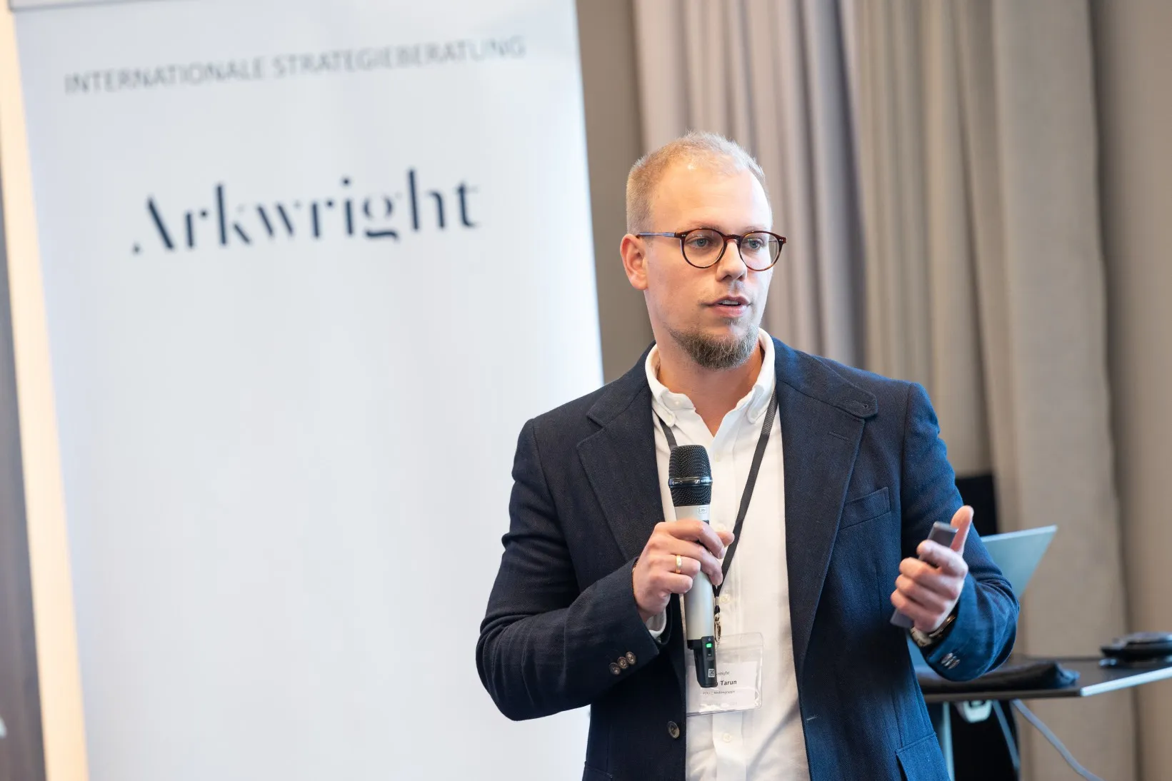 Junger Mann in blauem Sakko steht in einem Konferenzraum vorn und hält einen Vortrag