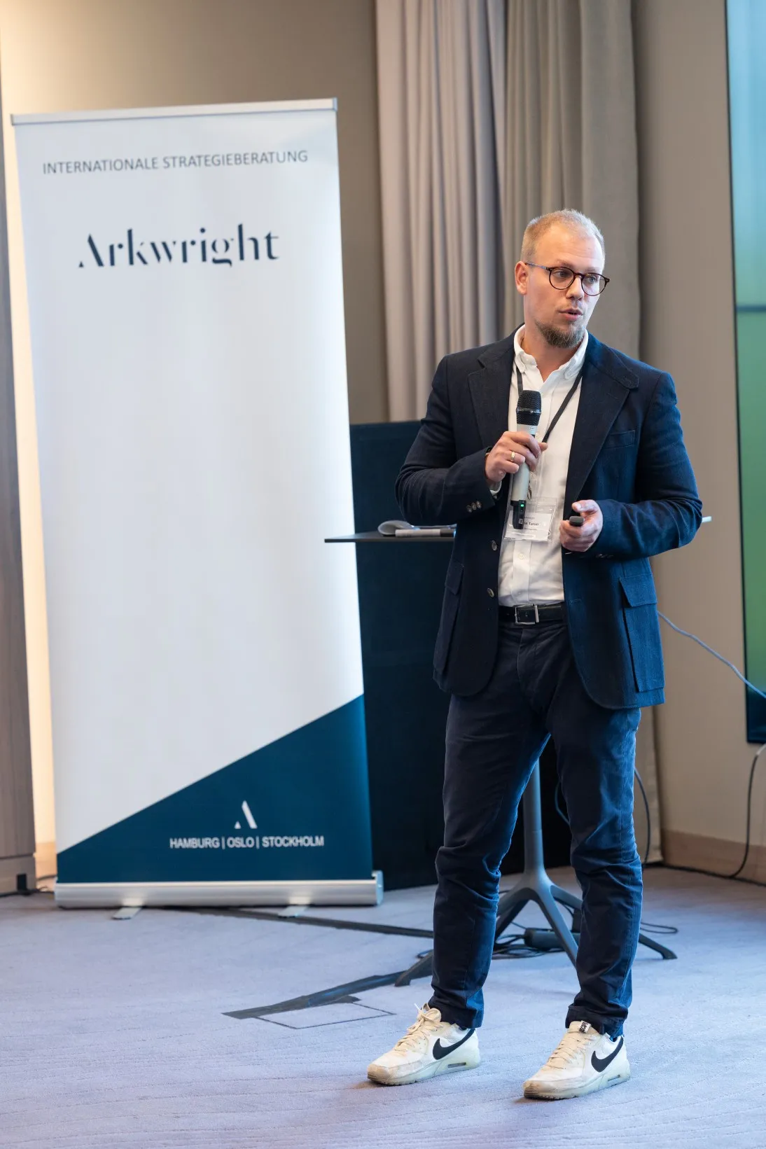 Junger Mann in blauem Sakko steht in einem Konferenzraum vorn und hält einen Vortrag