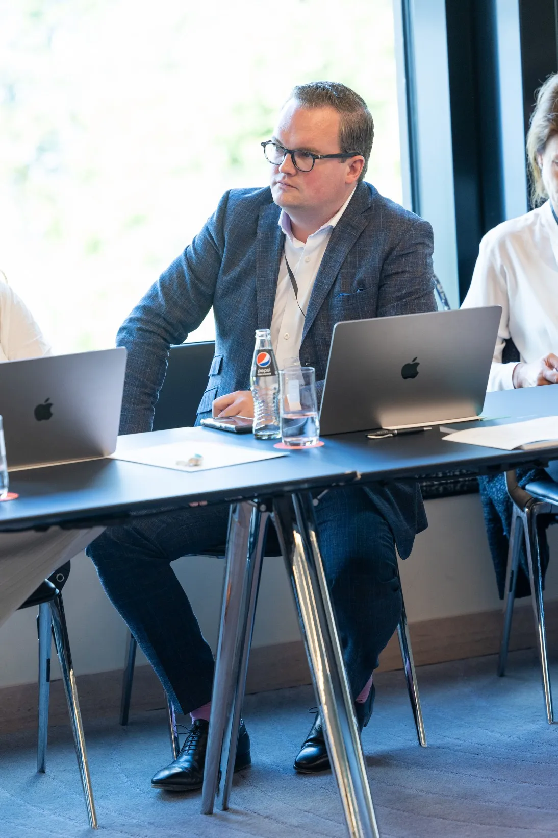 Mann sitzt vor seinem Macbook in einer Konferenz und hört Vortrag zu