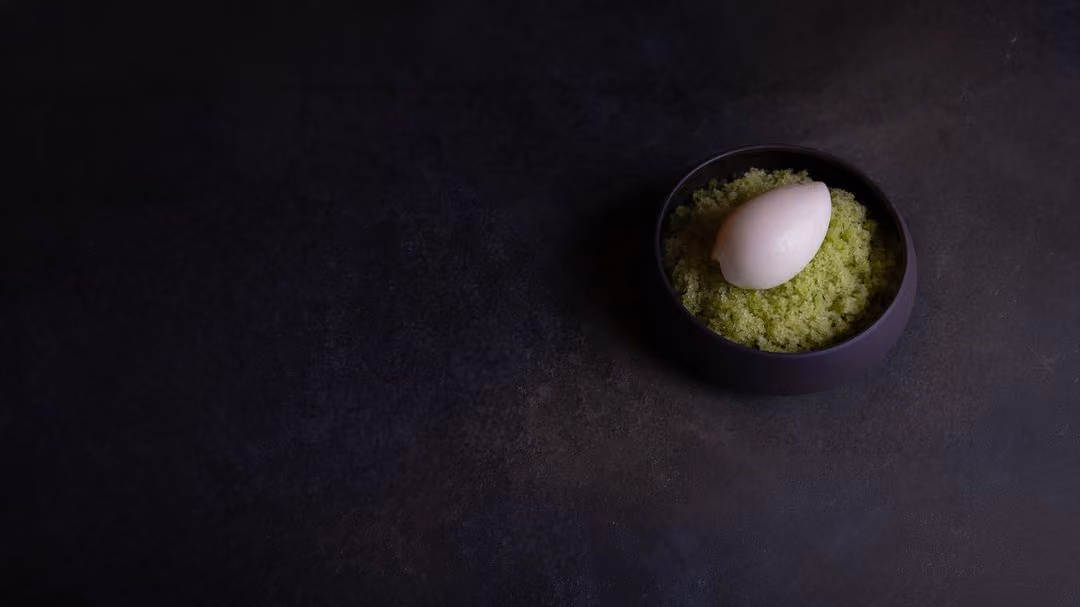 Scoop of pale pink sorbet on bright green shaved ice in a dark bowl