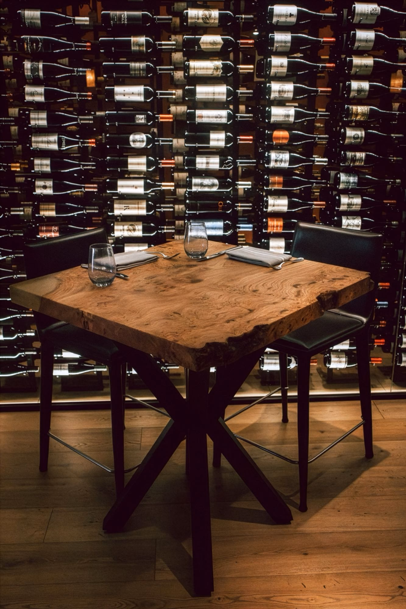 A table for two with a live-edge wood top beneath a floor-to-ceiling wall of racked wine bottles