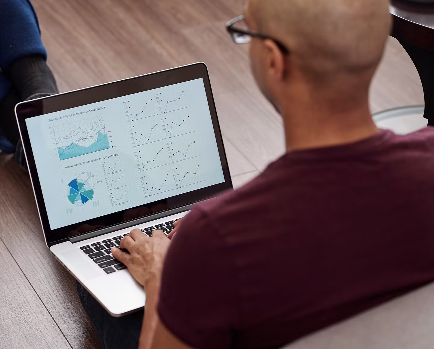 A person with glasses works on a laptop showing multiple data charts and graphs, analyzing business activity and performance metrics.