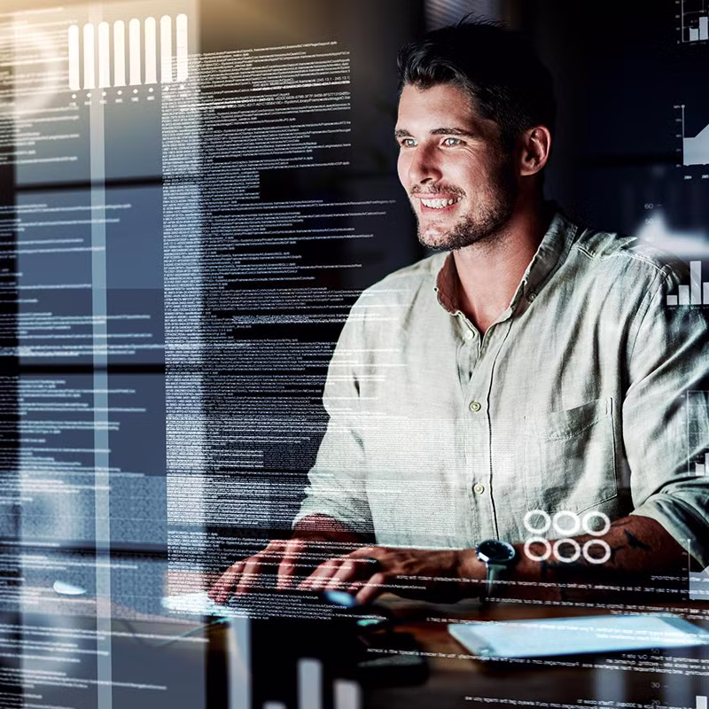 A man smiles while working at a computer surrounded by digital overlays of code, graphs, and analytics dashboards, symbolizing data lakes and big data management.
