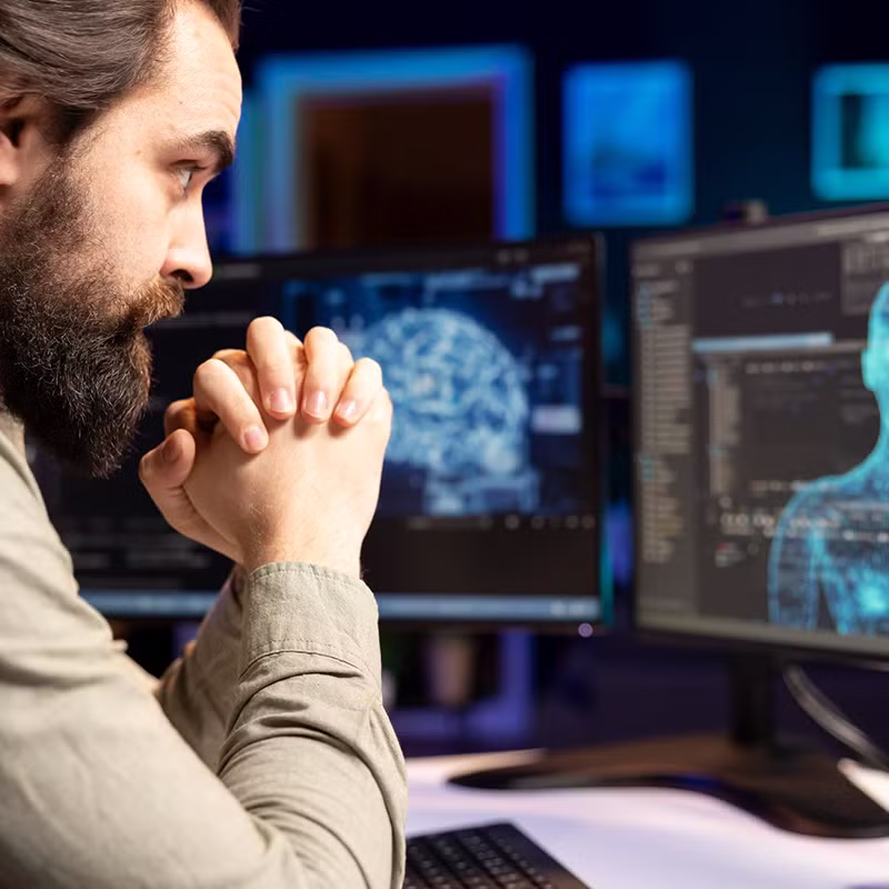 A man focuses on computer monitors displaying a digital human model and neural data visualizations, representing custom AI model development.