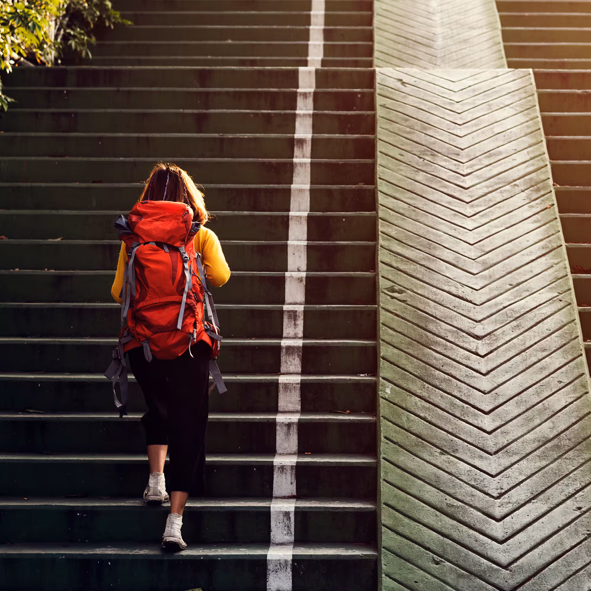 Person with backpack walking up stairs, representing progress, growth, and a clear path toward achieving goals.