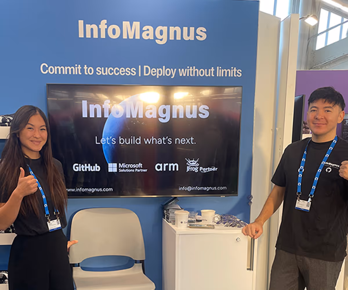 Two people giving thumbs up beside an InfoMagnus booth with a screen and promotional materials.