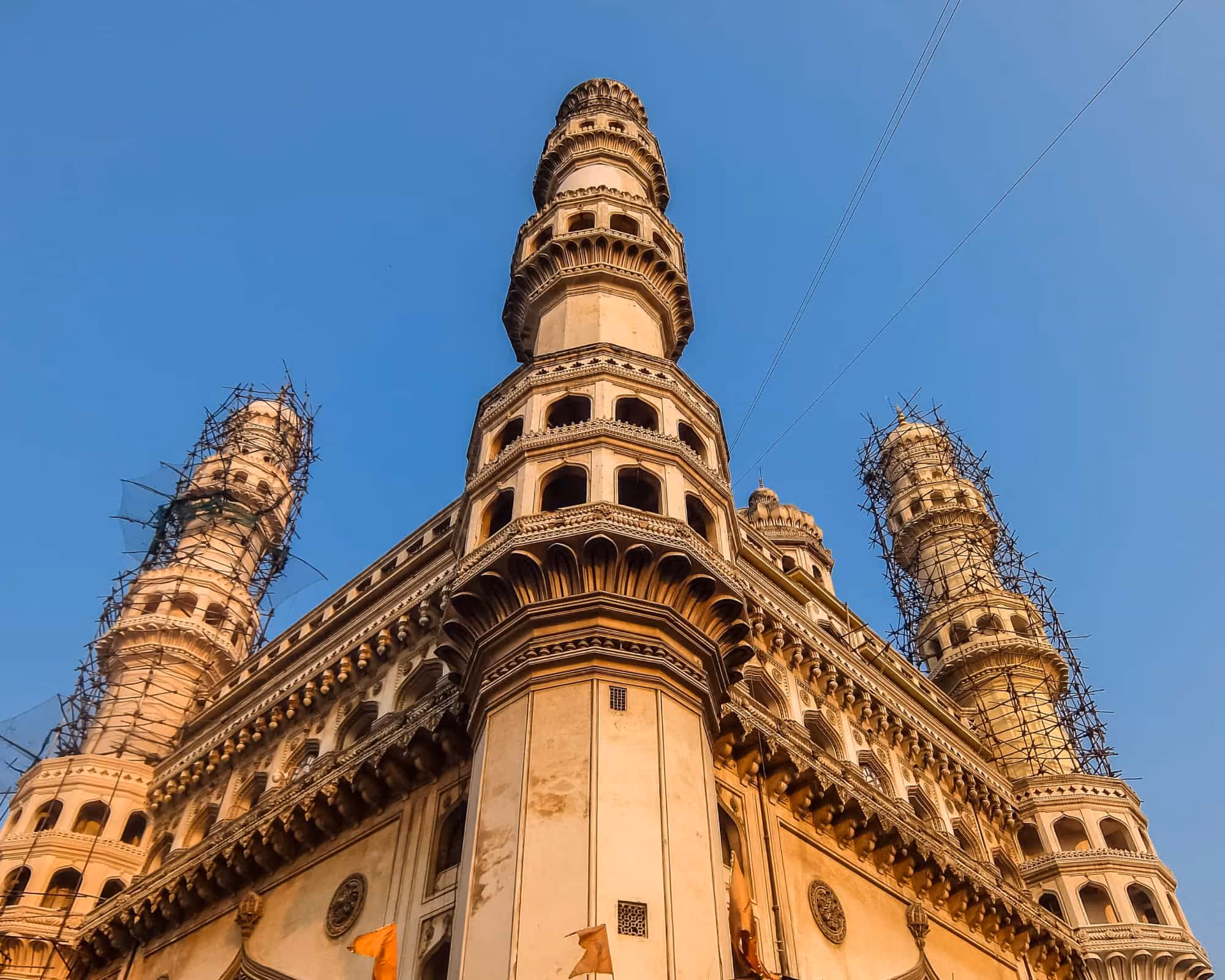 Low-angle view of historic Charminar monument with four minarets against clear blue sky.