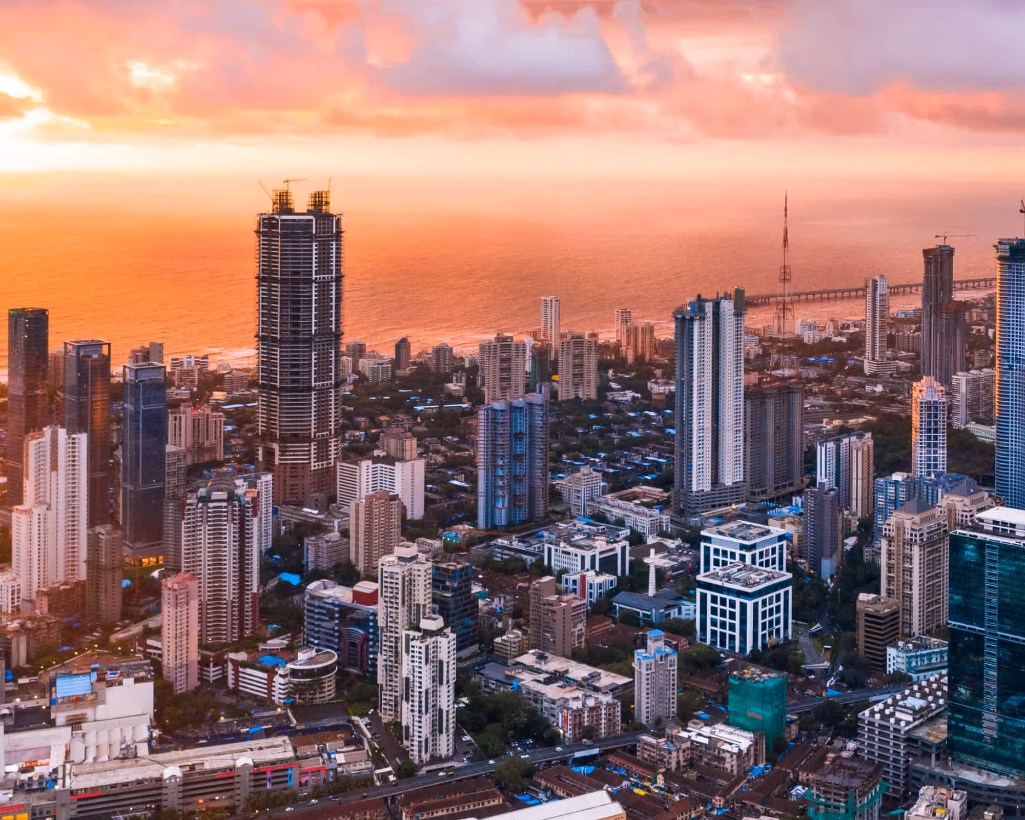 City skyline at sunset with high-rise buildings and an orange sky over the ocean.