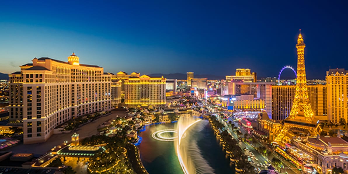 Aerial night view of Las Vegas Strip with Bellagio fountains, Eiffel Tower replica, and city lights.
