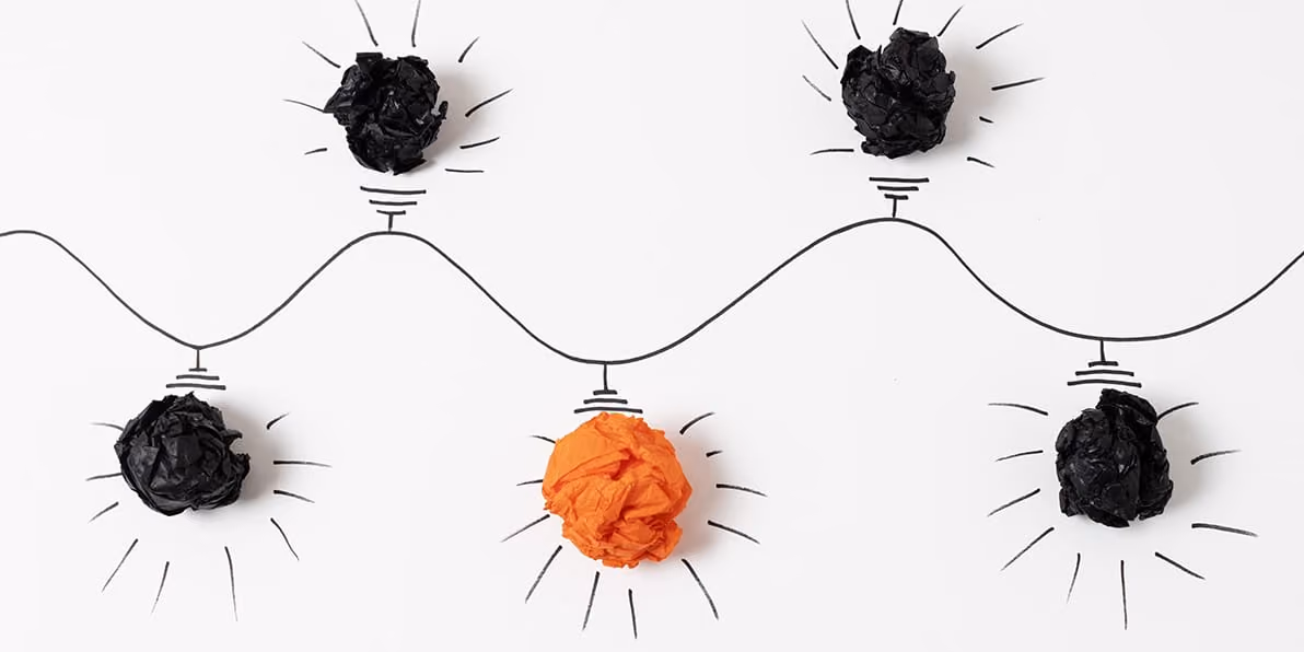Black and one orange crumpled paper balls with light rays drawn around them on white background.