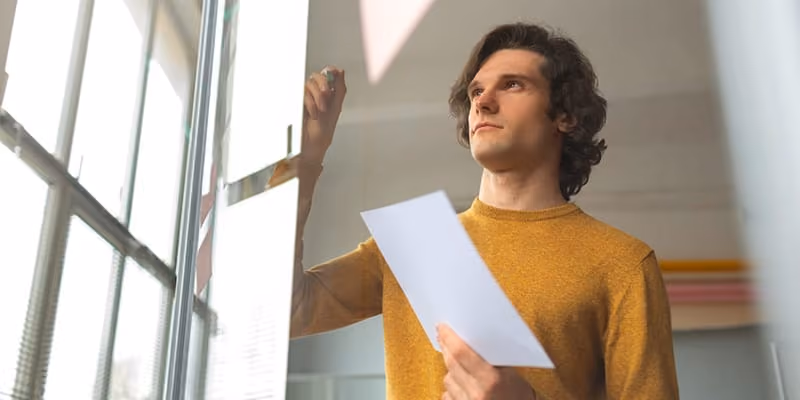 A man wearing a yellow shirt working on a diagram.