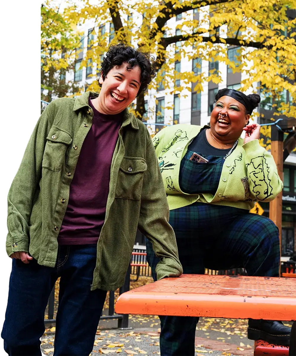 Two people stand side by side, laughing and smiling for a picture outdoors.