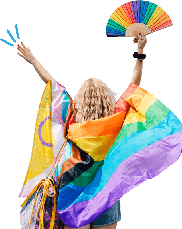 A woman holding a rainbow flag and a fan, smiling brightly in a vibrant outdoor setting.