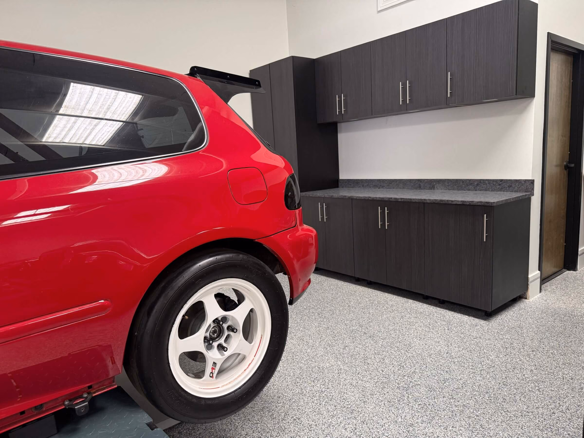 Custom garage cabinets and countertop behind a red car on a flake epoxy garage floor