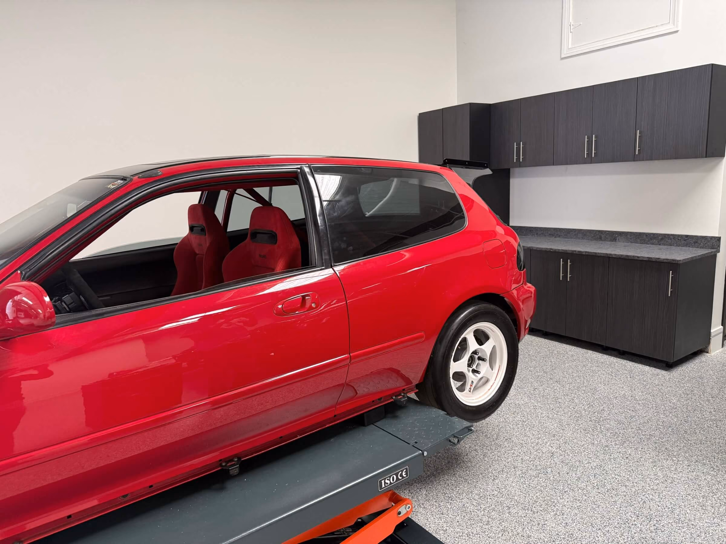 Red car on a lift beside custom wall and base garage cabinets on a flake epoxy floor