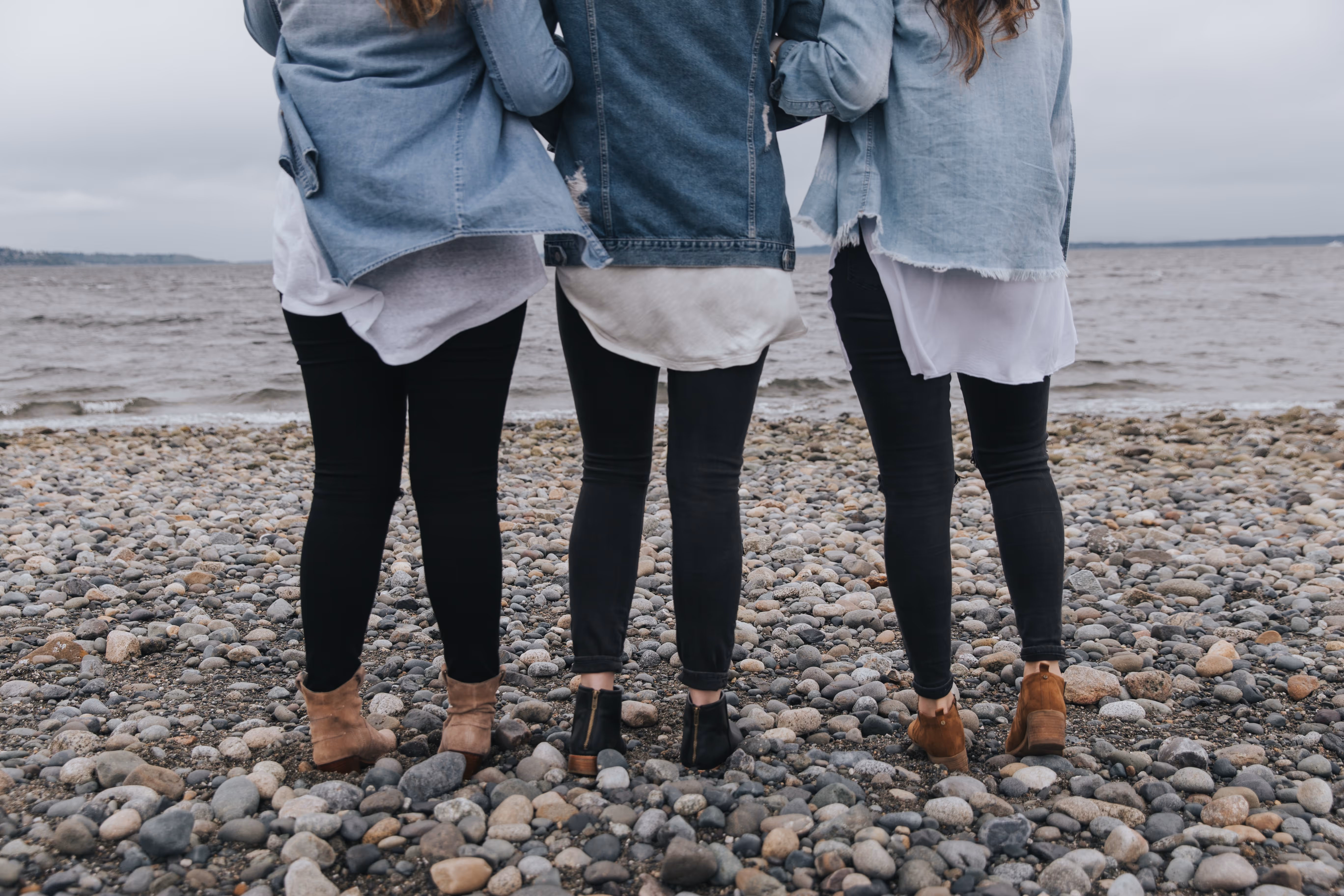 an image of three women holding hands and look out at the sea