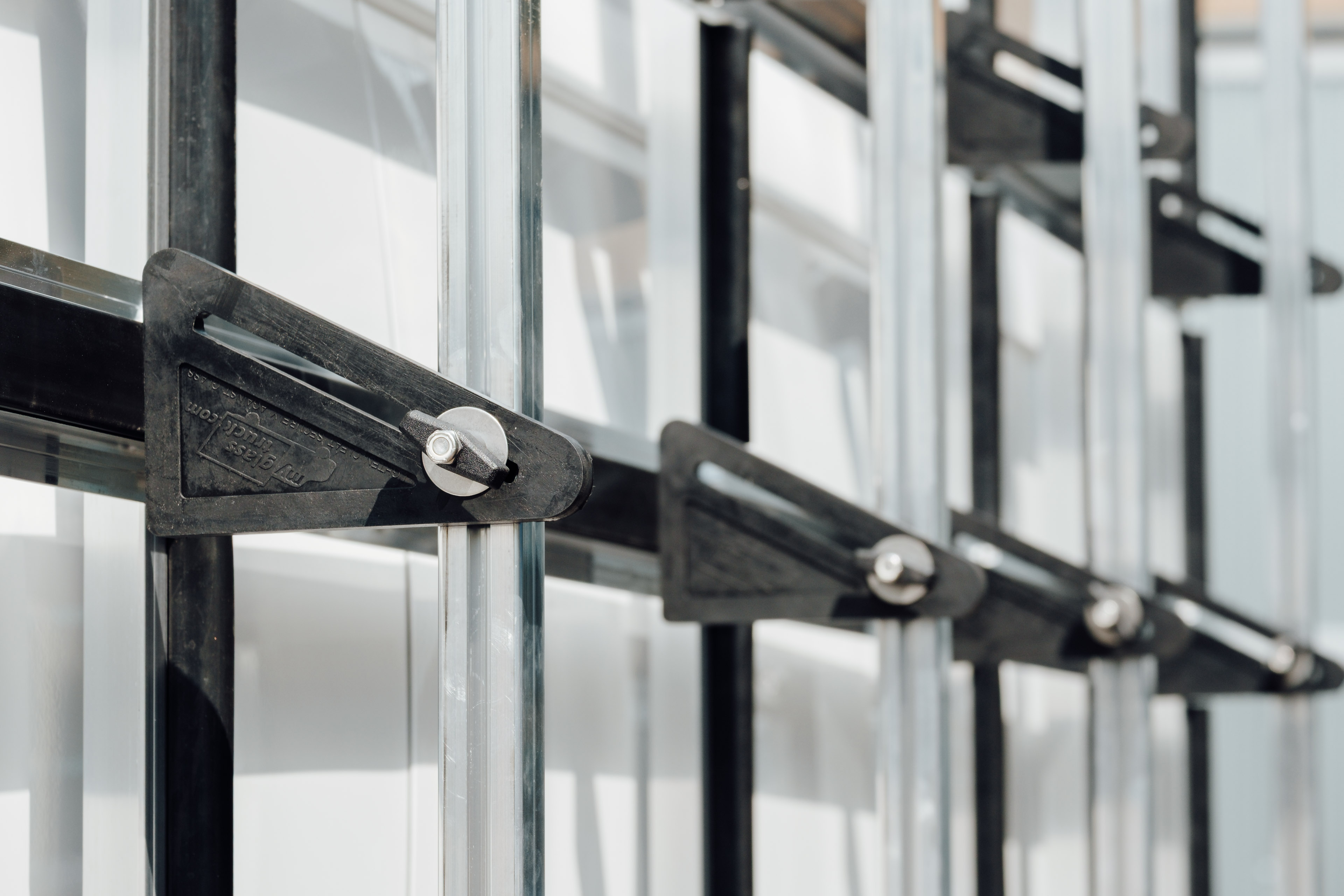 Close-up view of adjustable poles on a glass rack, showing the rubber contact pads and aluminum vertical posts.