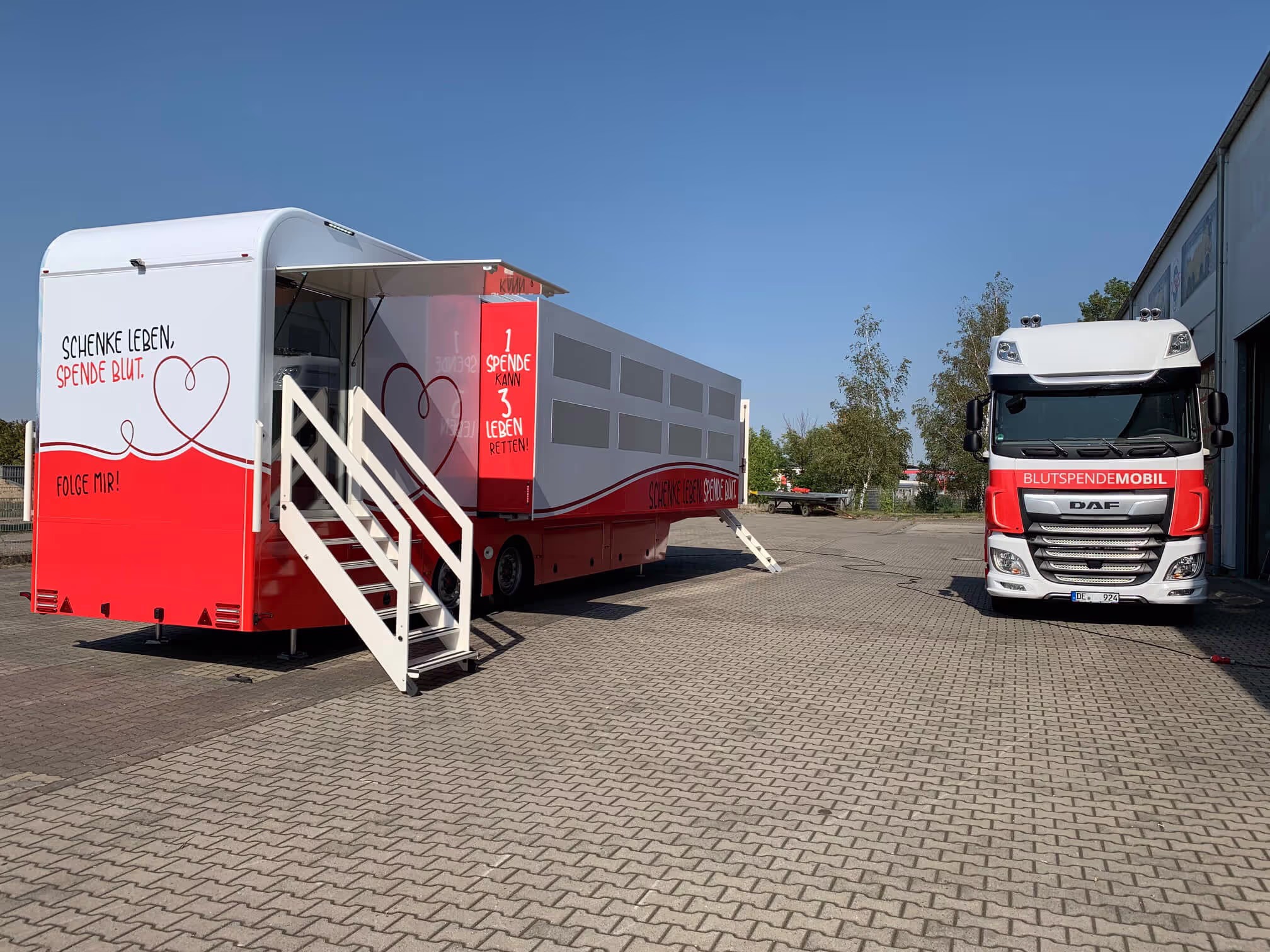 Blood donation mobile vehicles with red and white branding parked on brick ground.