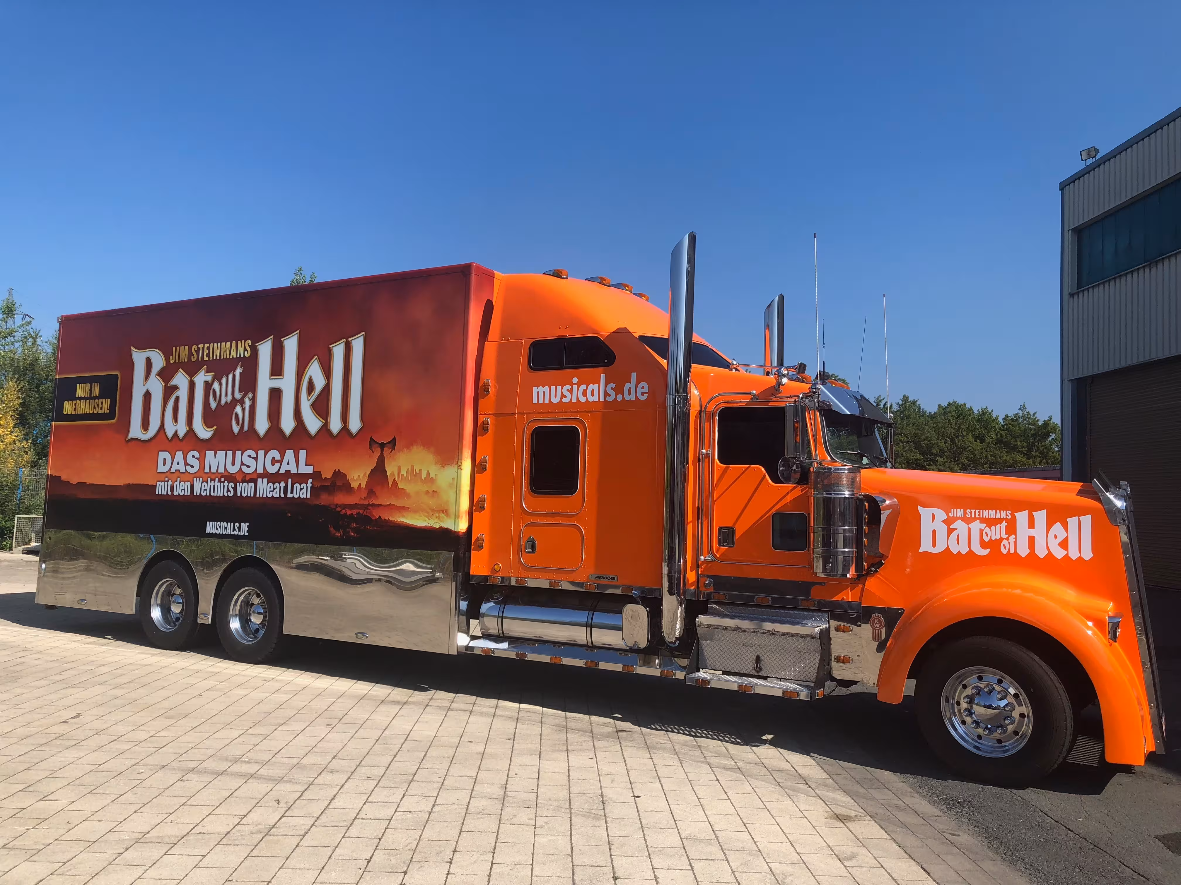 Orangener Promotiontruck mit Bat out of Hell Musical-Werbung auf Parkplatz.