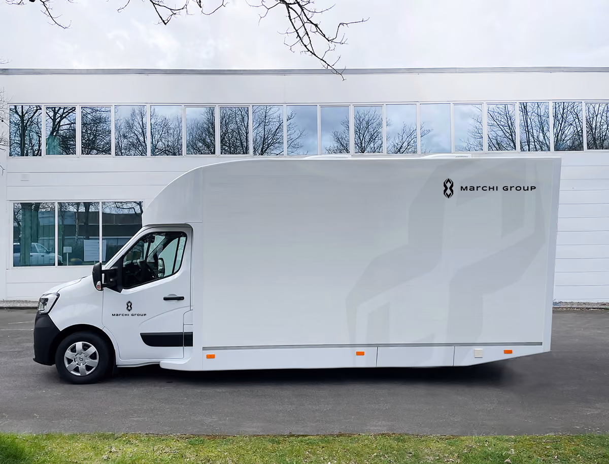 White Marchi Drive van with Marchi Group branding parked in front of modern building.