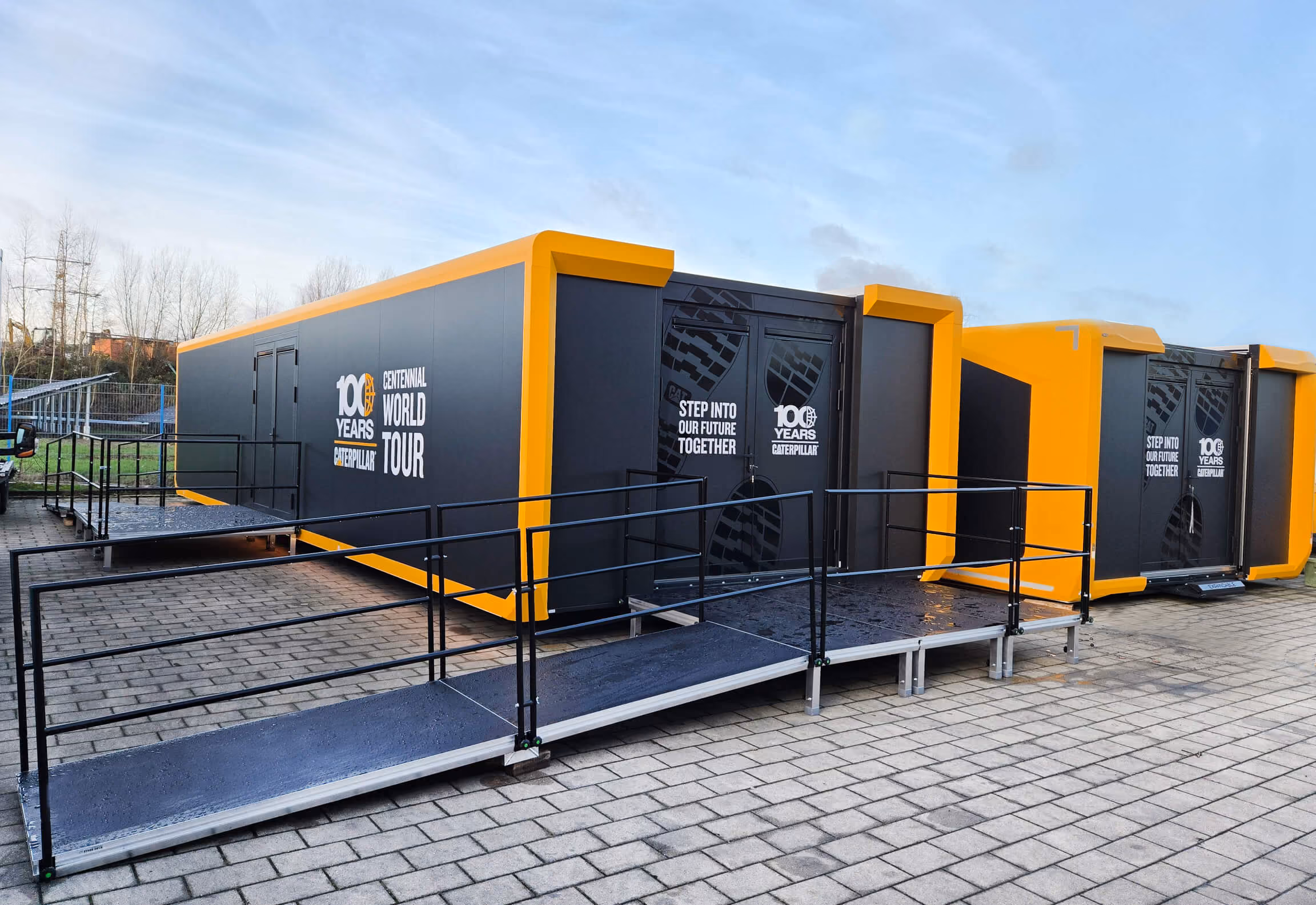 Schwarze und gelbe Ausstellungscontainer mit "100 Years Caterpillar" Branding auf gepflastertem Platz