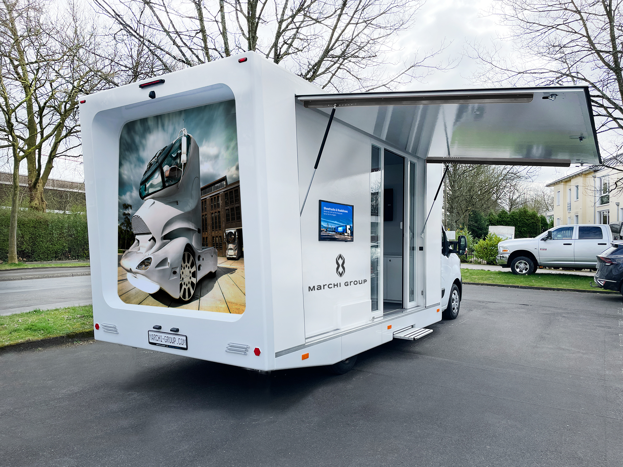 Weißer Marchi Drive Info Van mit Marchi Group Branding auf der Rückseite und ausgeklappter Seite. 