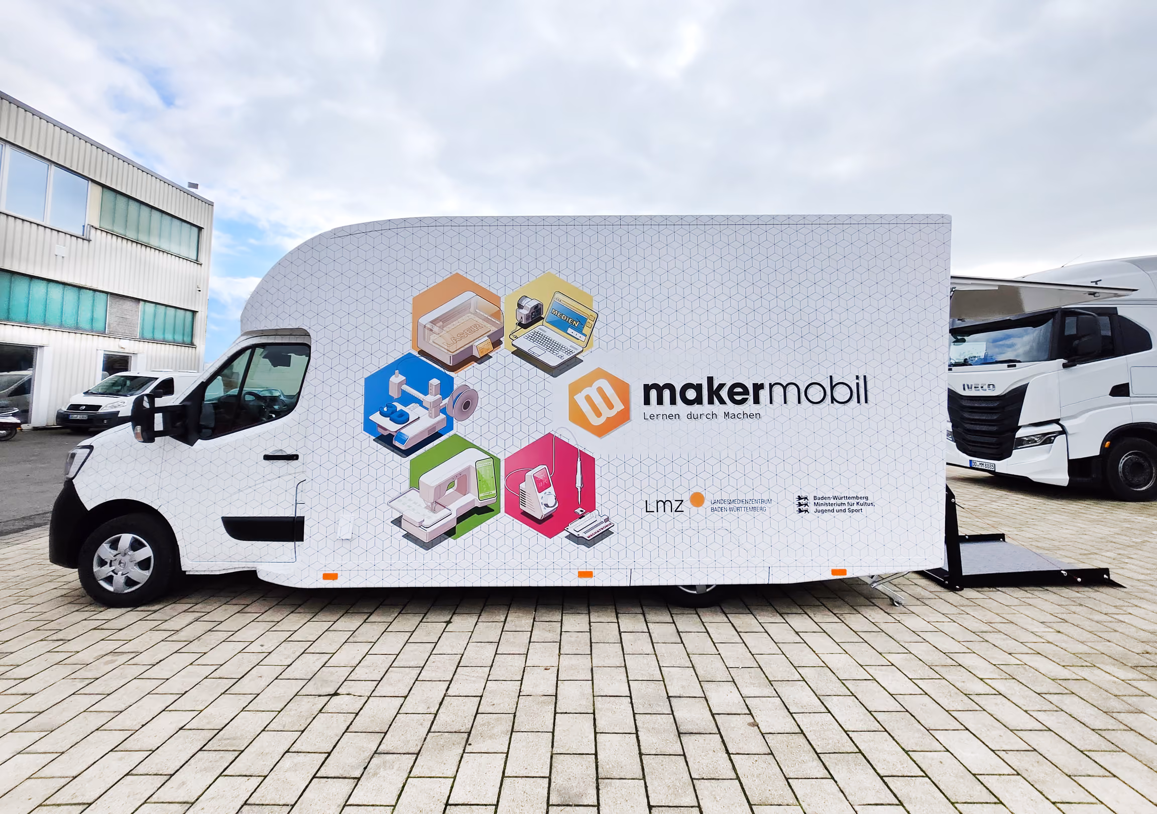 White makermobil educational "Marchi Drive" van with colorful graphics and icons parked outdoors.