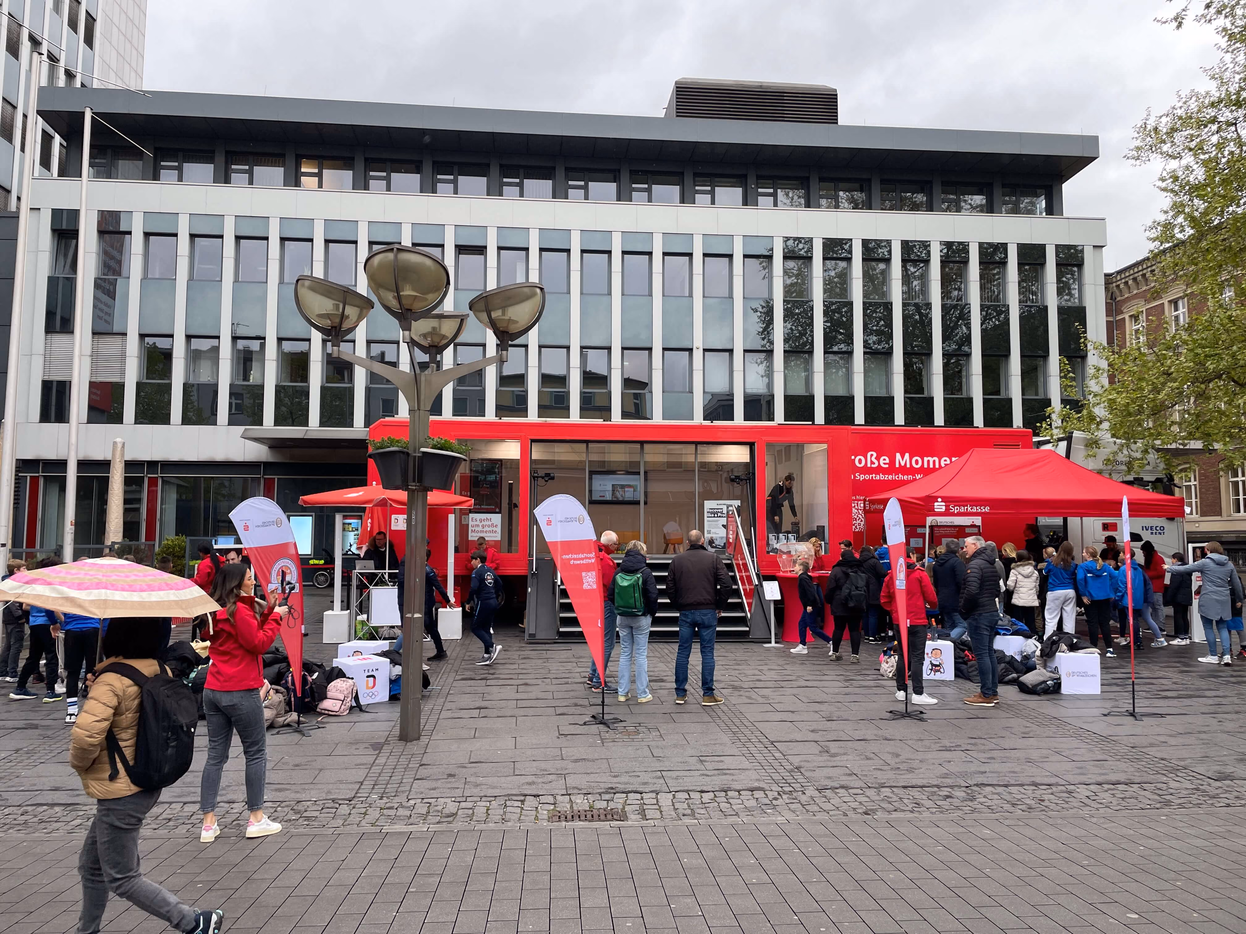 Sparkasse Showroom Mini-Truck mit Besuchern auf öffentlichem Platz vor modernem Bürogebäude.
