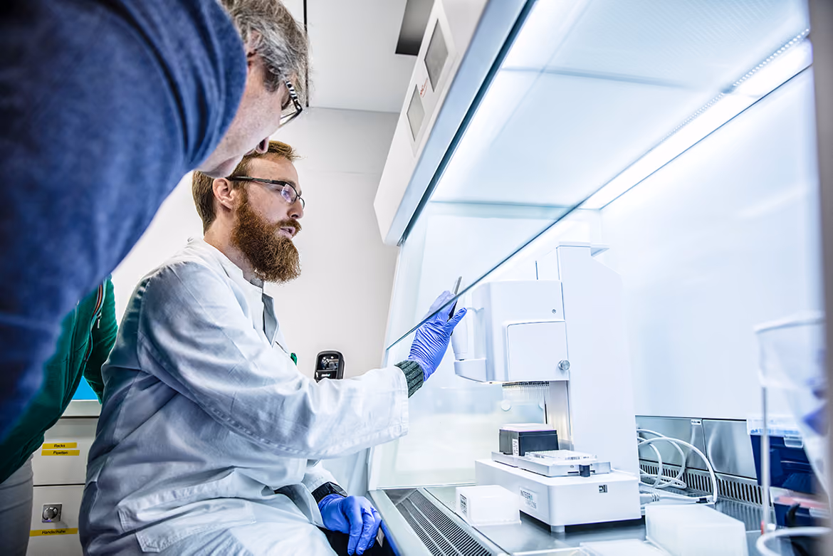 Scientist in white lab coat and blue gloves working in a well lit modern laboratory with analytical equipment.
