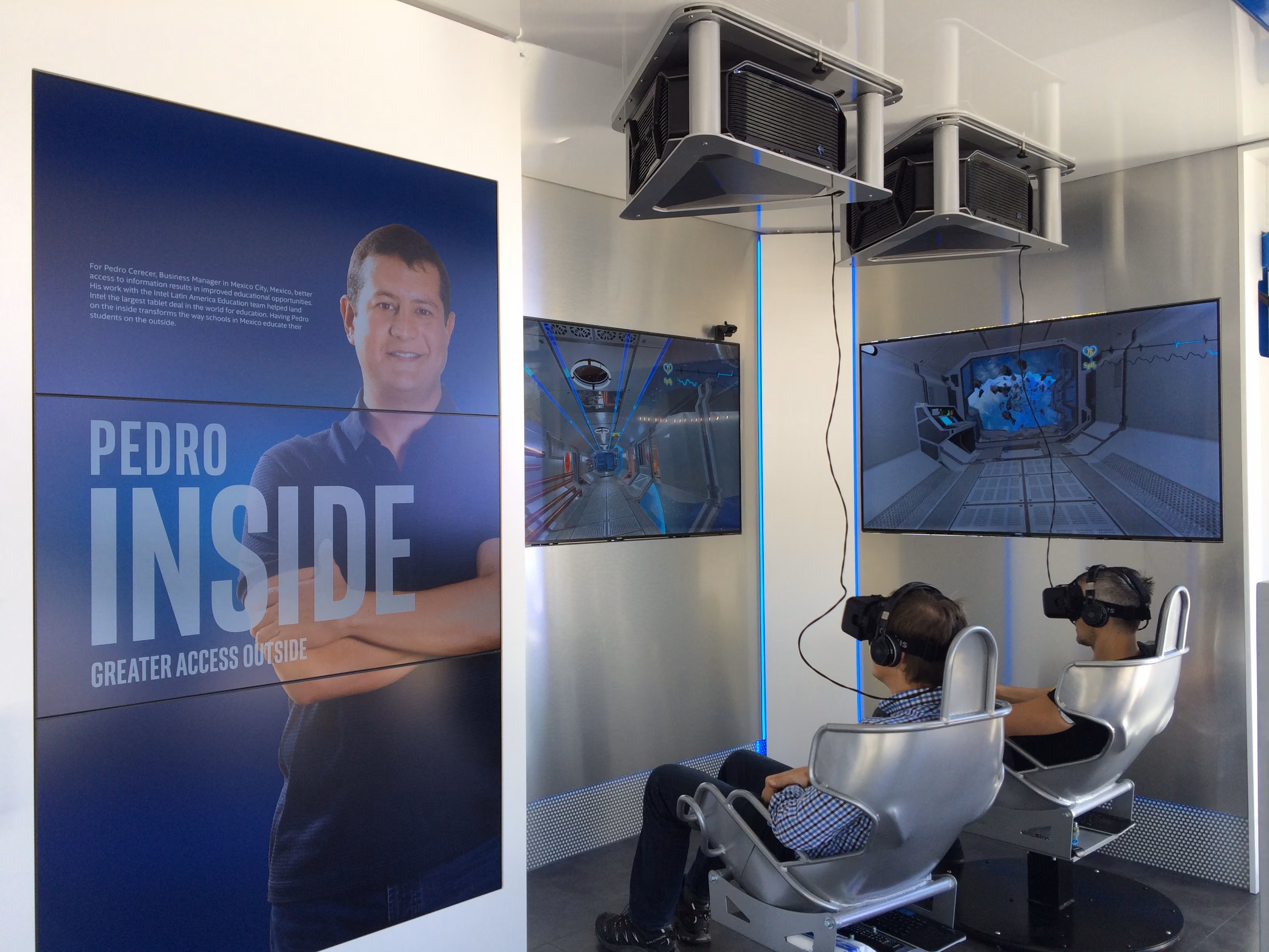 Zwei Personen tragen VR-Headsets und betrachten sitzend aktive Displays im Intel Showcontainer.