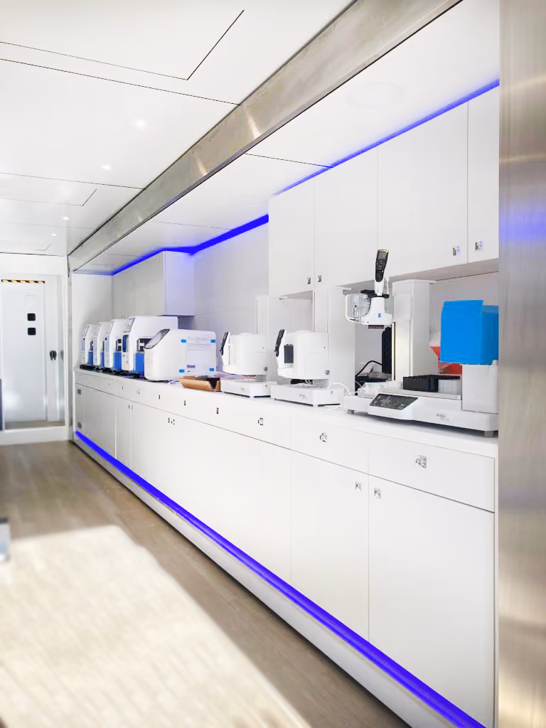 A modern laboratory with a wall of cupboards, white appliances and blue LED lighting on the walls and ceiling.