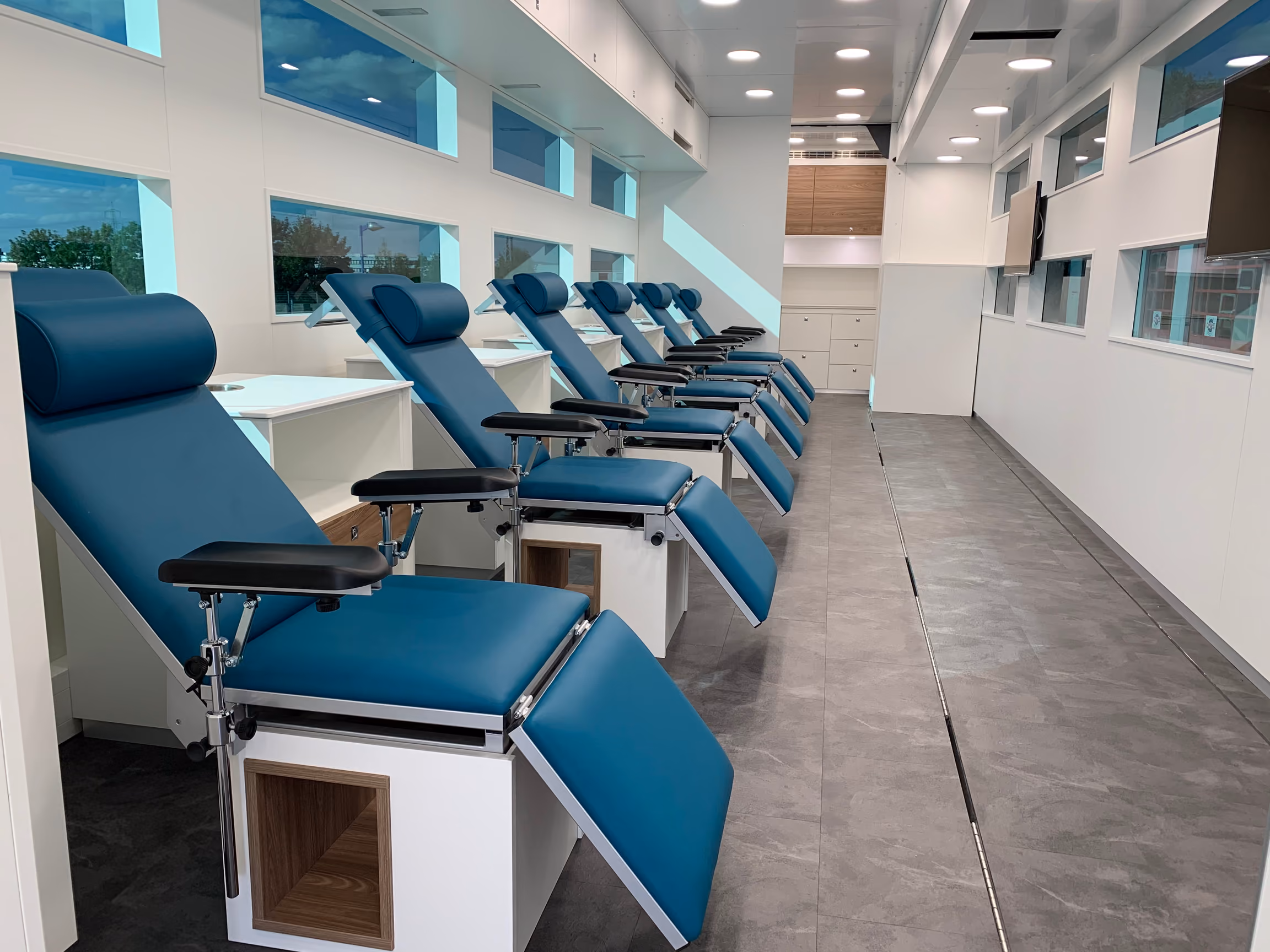 Blood donation truck interior with blue reclined donor chairs and big windows.
