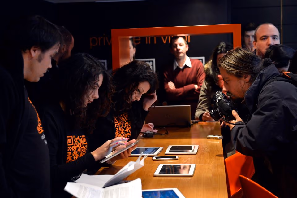 Gruppe von Menschen sitzt an Holztisch mit Tablets und Laptops bei Präsentation.