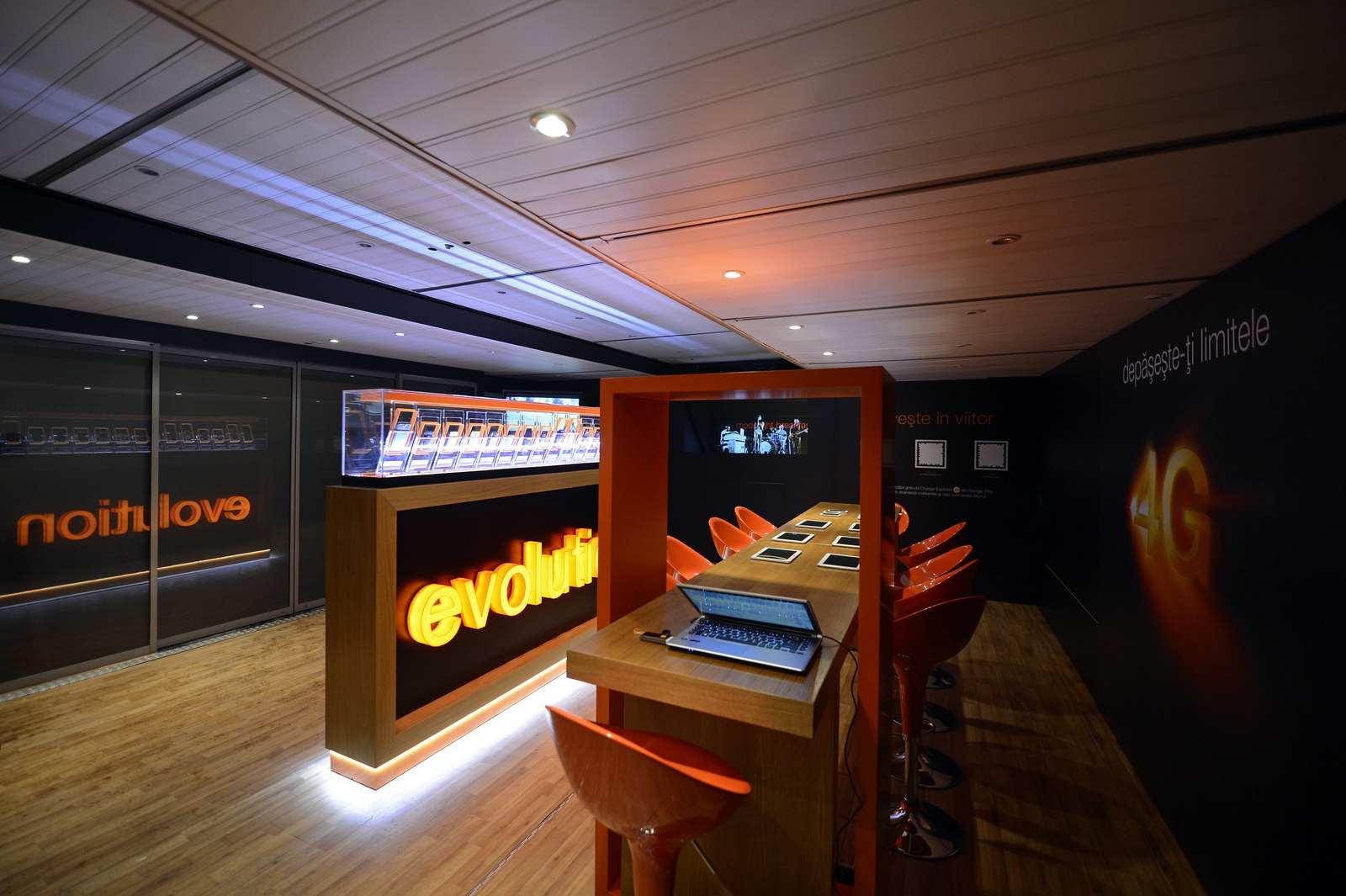 Innenraum des mobilen Showroom-Trucks von Mobilfunkanbieter Orange: Ausstellungsraum mit orangenen Displays, leuchtenden Schildern und interaktiven Ausstellungstresen.